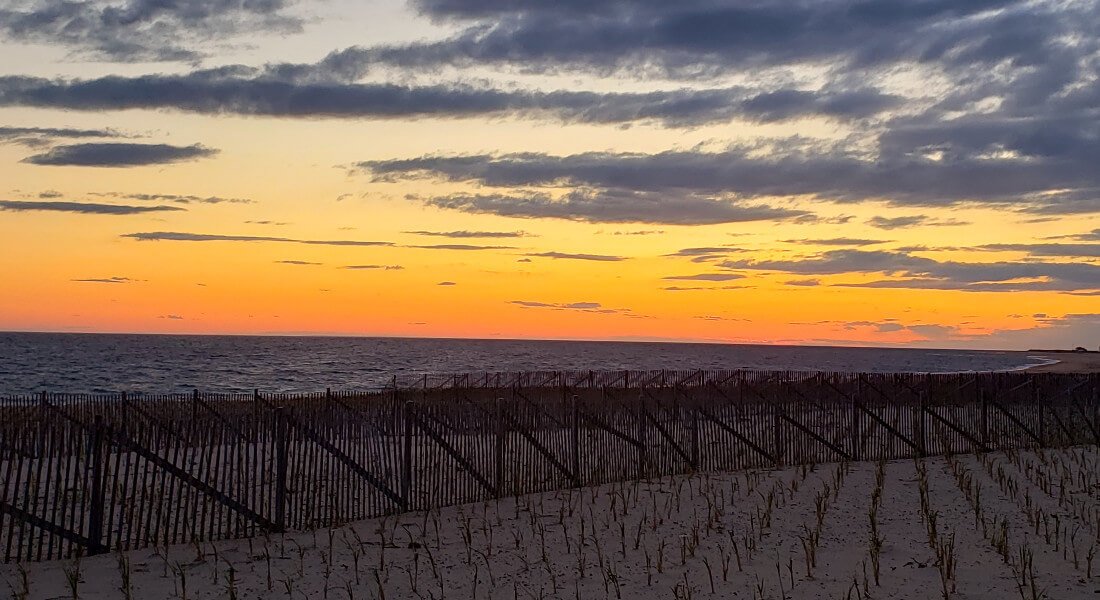 sunset at Race point with rippling ocean waves, and gray clouds sand fence between ocen and beach